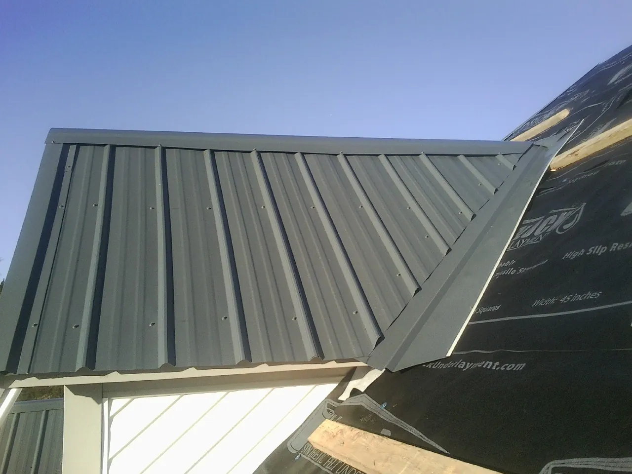 Gray metal roof panels going on over a garage gable in Plymouth